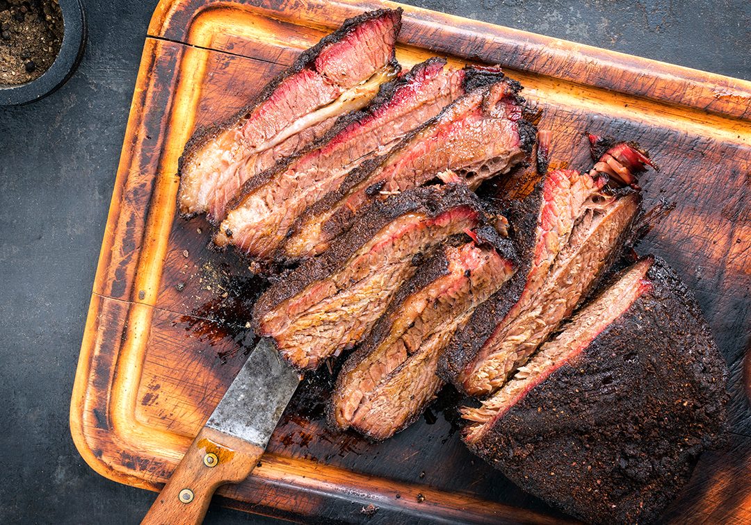 Traditional smoked barbecue wagyu beef brisket as piece and sliced offered as top view on an old cutting board with copy space left